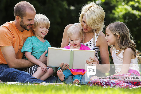 'A family with three children sit on the grass reading a book; Oregon  United States of America'