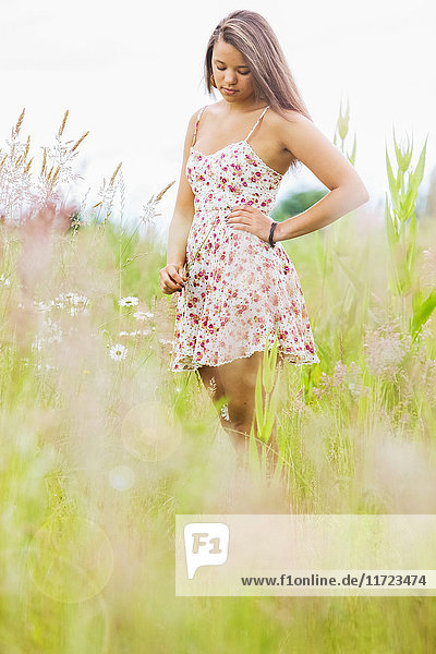 'A young woman stands looking contemplative in a field of wildflowers and tall grasses; Oregon  United States of America'