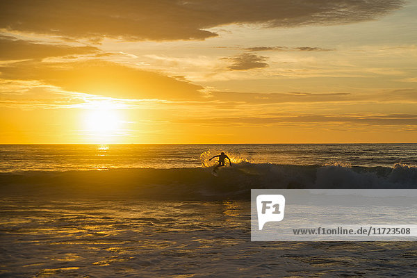 Surfer  der bei Sonnenuntergang auf einer Welle reitet  Dreamland Strand; Insel Bali  Indonesien'.