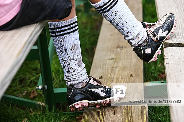 'A soccer player sitting on wooden stands wearing cleats and mud splashed socks; Oregon  United States of America'