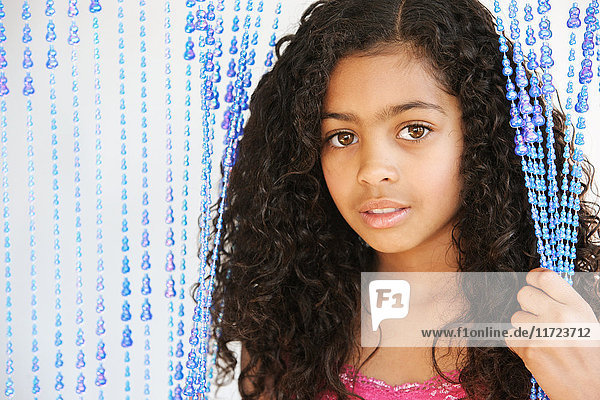 'Portrait of a young girl with dark  curly hair and brown eyes standing and holding strings of a beaded curtain; Vancouver  Washington  United States of America'