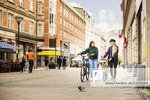 Two young women walking and pushing bicycles in old town