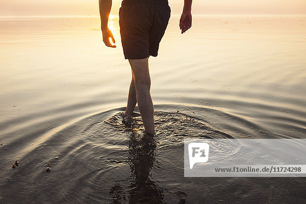 Mann in kurzen Hosen watet im Meer bei Sonnenuntergang