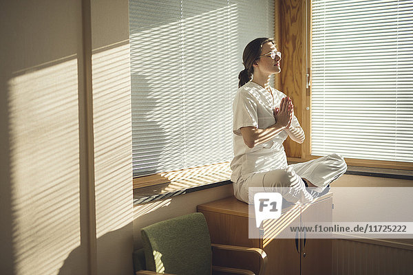 Female doctor meditating by window