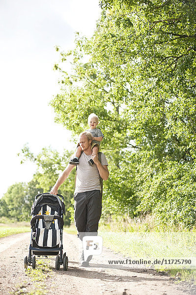 Man pushing with pram carrying son on shoulders