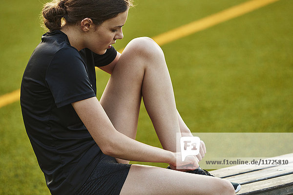 Teenager-Mädchen bindet Schnürsenkel  während sie auf einer Bank im Spielfeld sitzt