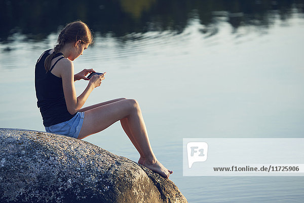 Teenage girl sitting and using cell phone by lake