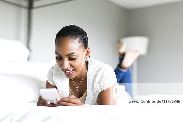 Frau liegt auf dem Bett und benutzt ein Smartphone