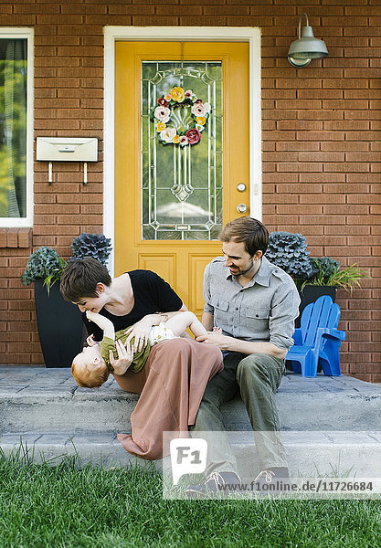 Parents with daughter (12-17 months) sitting in front of house