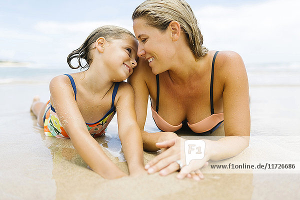 Mother lying with daughter (6-7) on beach