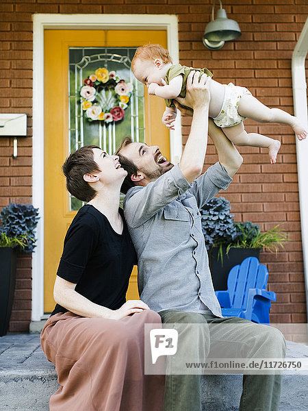 Eltern mit Tochter (12-17 Monate) vor dem Haus sitzend