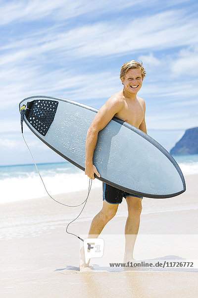 Mann geht am Strand und hält Surfbrett