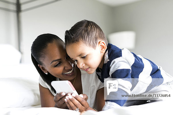 Mother and son (2-3) lying on bed and using smart phone