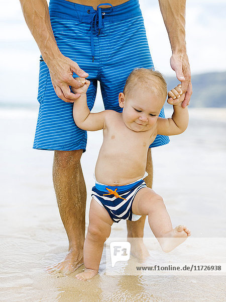 Sohn (12-17 Monate) lernt mit Vater am Strand laufen
