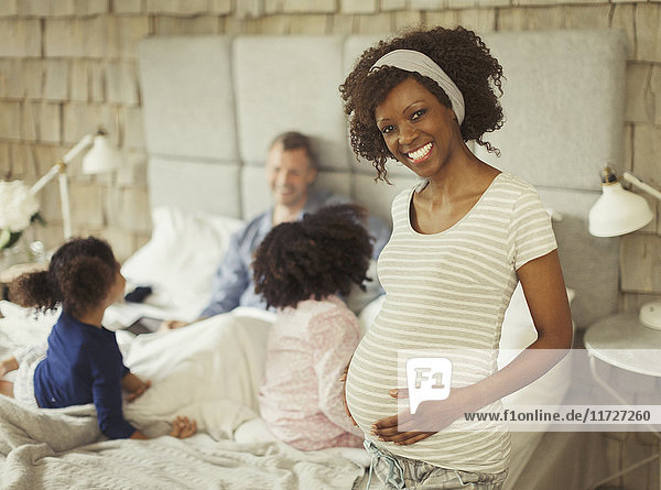 Portrait lächelnde schwangere Frau im Schlafzimmer mit junger Familie