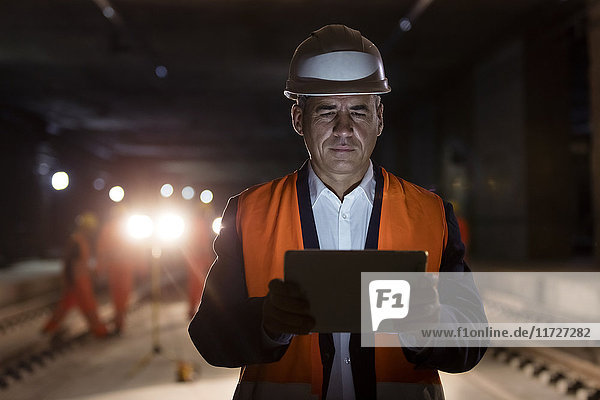Seriöser Vorarbeiter mit digitalem Tablett auf dunkler Baustelle