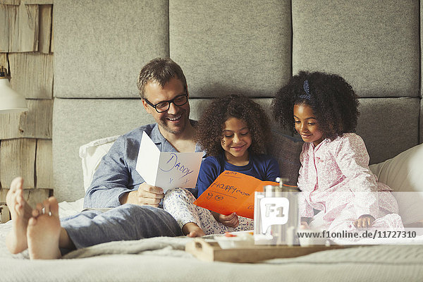 Multi-ethnic daughters giving cards to father on bed on Father’s Day