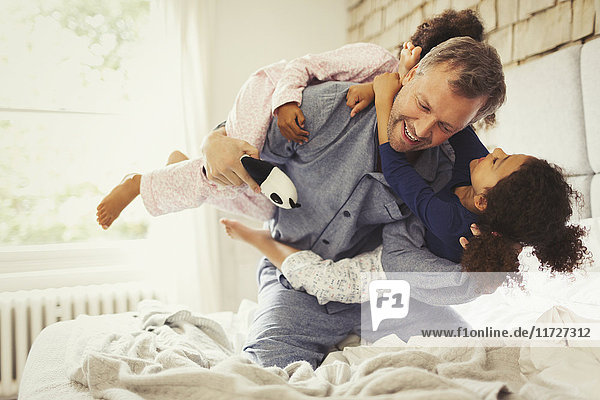 Multi-ethnic daughters playing and tackling father on bed