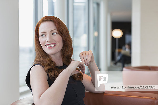 Lächelnde Geschäftsfrau mit roten Haaren über die Schulter schauend in der Lounge