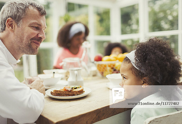 Multi-ethnic father and daughter playing staring game at kitchen table