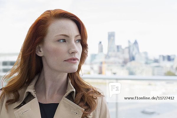 Portrait nachdenkliche Geschäftsfrau mit roten Haaren auf dem Stadtbalkon