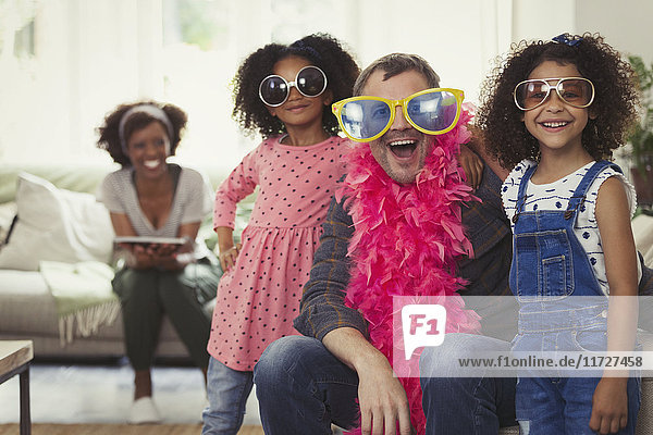 Portrait playful multi-ethnic father and daughters playing dress up with sunglasses and feather boas