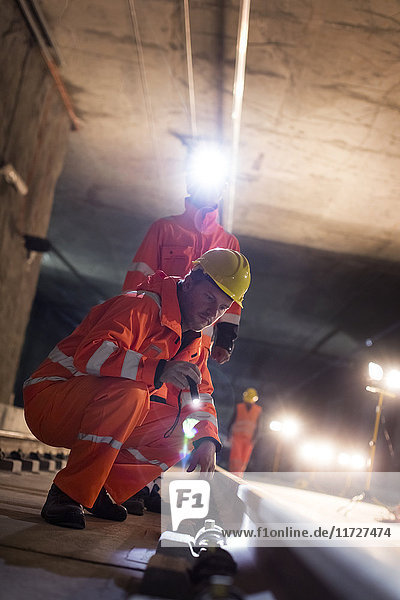 Bauarbeiter untersuchen unterirdische Gleise auf dunkler Baustelle