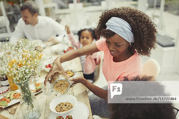 Mother pouring granola cereal for daughter at breakfast table