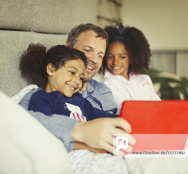 Multi-ethnischer Vater und Töchter mit digitalem Tablett auf dem Bett