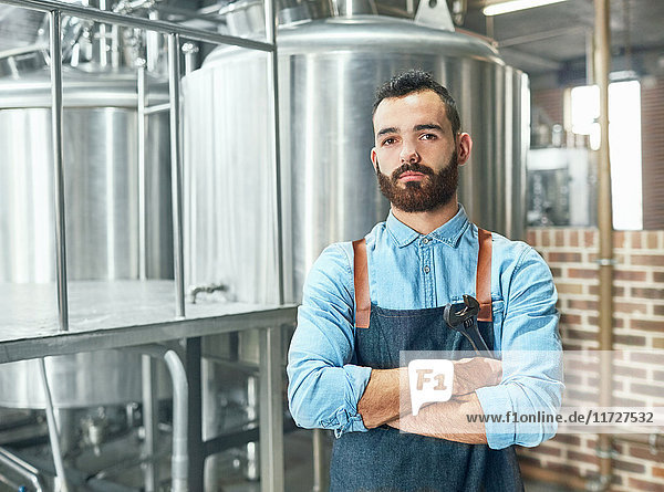 Portrait confident male brewer in front of vat in brewery