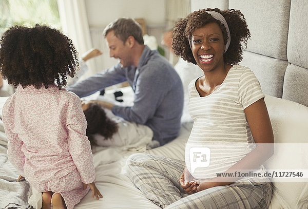 Portrait laughing pregnant woman with young family on bed