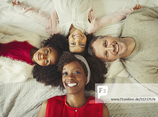 Overhead portrait smiling multi-ethnic young family laying on bed