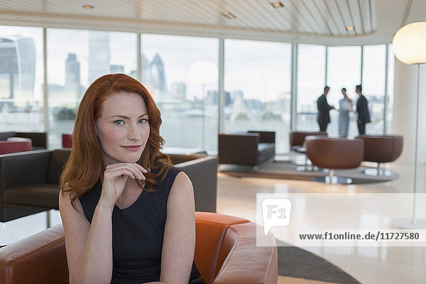 Portrait selbstbewusste Geschäftsfrau mit roten Haaren in urbaner Hochhaus-Bürolounge