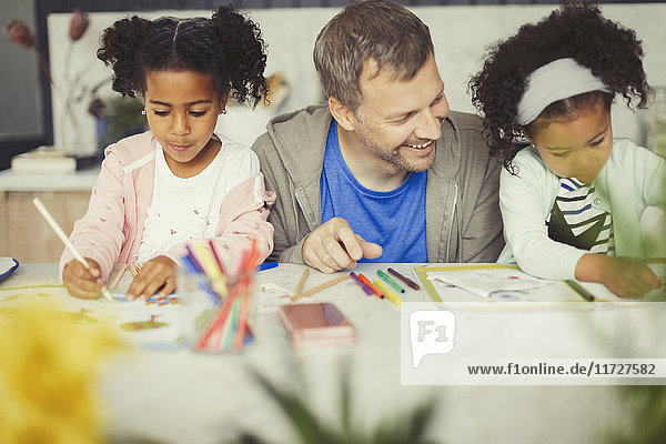 Multi-ethnic father and daughters coloring with markers at table