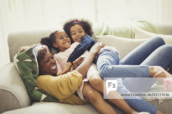 Verspielte Mutter und Töchter kuscheln auf dem Sofa