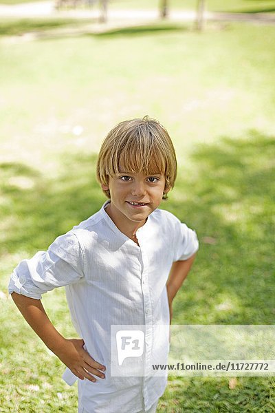Portrait of a cute blond boy in park smiling at camera