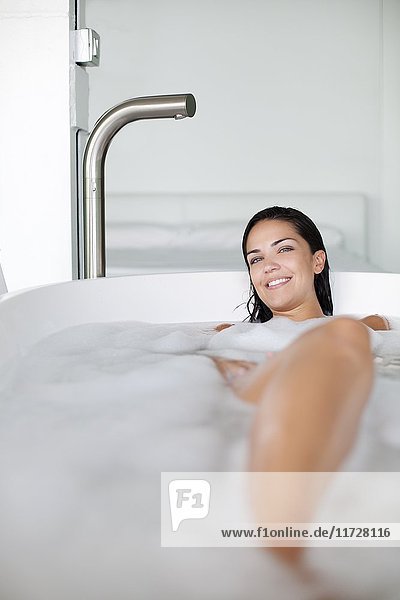 Young pretty brunette woman enjoying a bath and smiling at camera