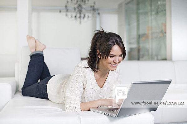 Schöne brünette Frau auf einer Couch mit Computer