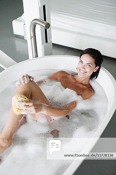 Junge hübsche brünette Frau genießt ein Bad und lächelt in die Kamera.