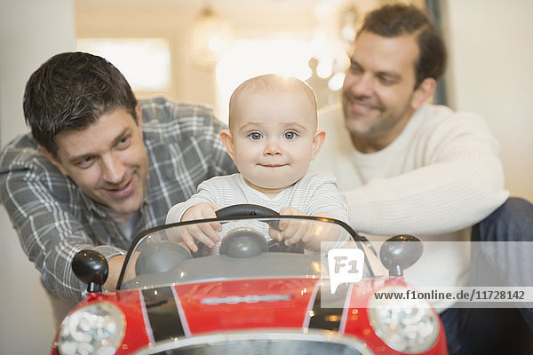 Portrait male gay parents pushing baby son in toy car