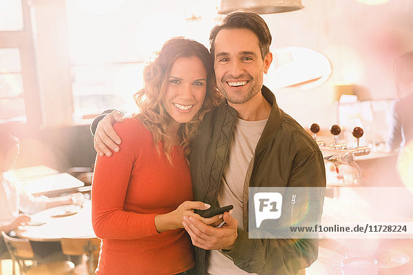 Porträt liebevolles lächelndes Paar  das in einer Bar ein Mobiltelefon benutzt