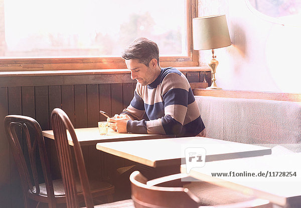 Man texting with cell phone at table in sunny cafe window