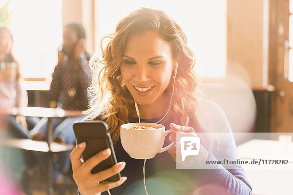 Frau mit Kopfhörern trinkt Cappuccino und chattet in einem Café