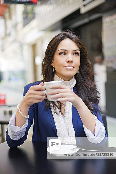 Porträt einer hübschen brünetten Frau beim Kaffee im Freien lächelnd