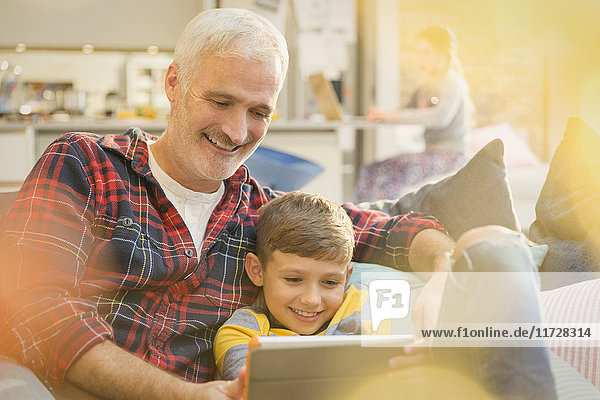 Vater und Sohn verbinden sich und teilen sich ein digitales Tablett auf dem Sofa.