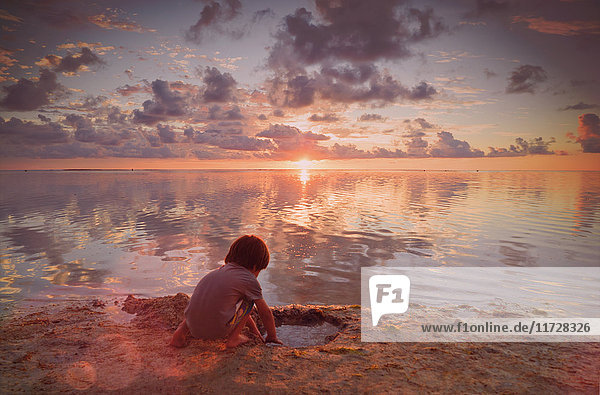 Junge spielt im nassen Sand am ruhigen Strand bei Sonnenuntergang