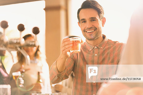 Porträt eines lächelnden Mannes  der an einer Bar mit einem Bierglas anstößt