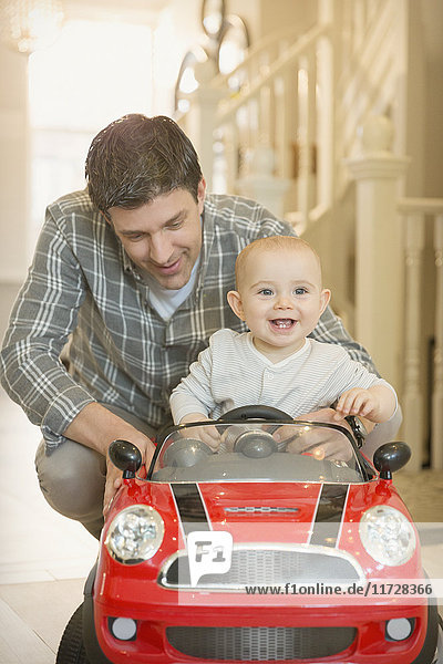 Vater schiebt fröhliches  süßes Baby im Spielzeugauto