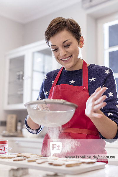 Smiling woman baking  sifting sugar over cookies in kitchen