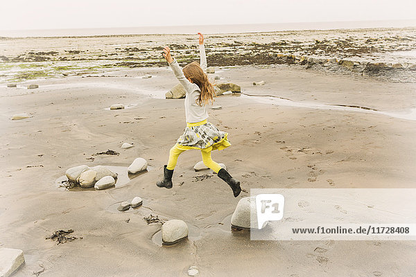 Übermütiges Mädchen springt vor Freude auf Strandfelsen